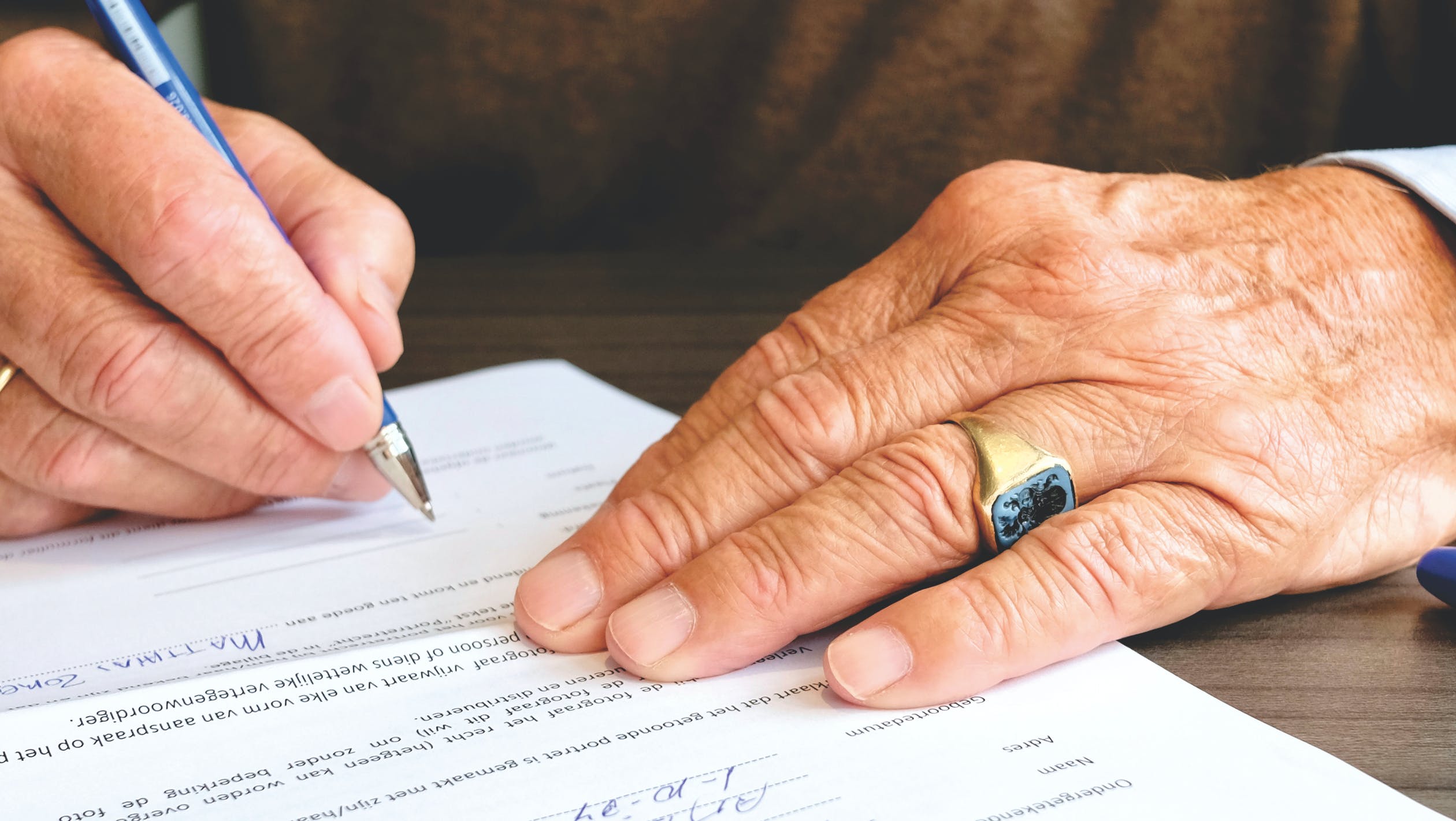 Eine Hand eines älteren Menschen unterschreibt einen Vertrag